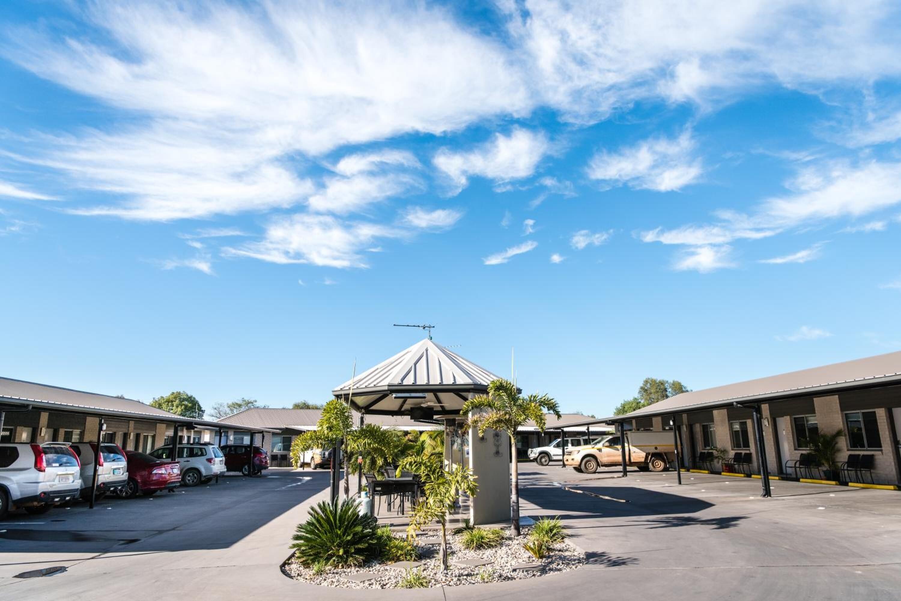 A motel with a central gazebo, parking lot, and multiple rooms.