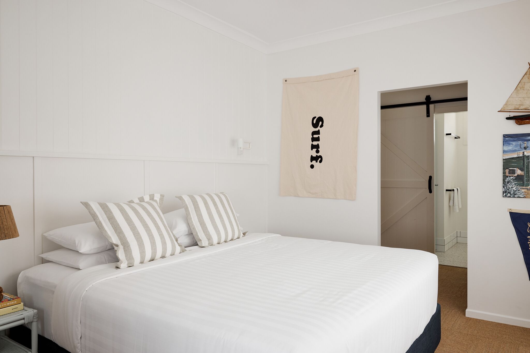 Ein Schlafzimmer mit einem großen Bett, weißen Wänden, einer Holztür und einem hängenden Schild.