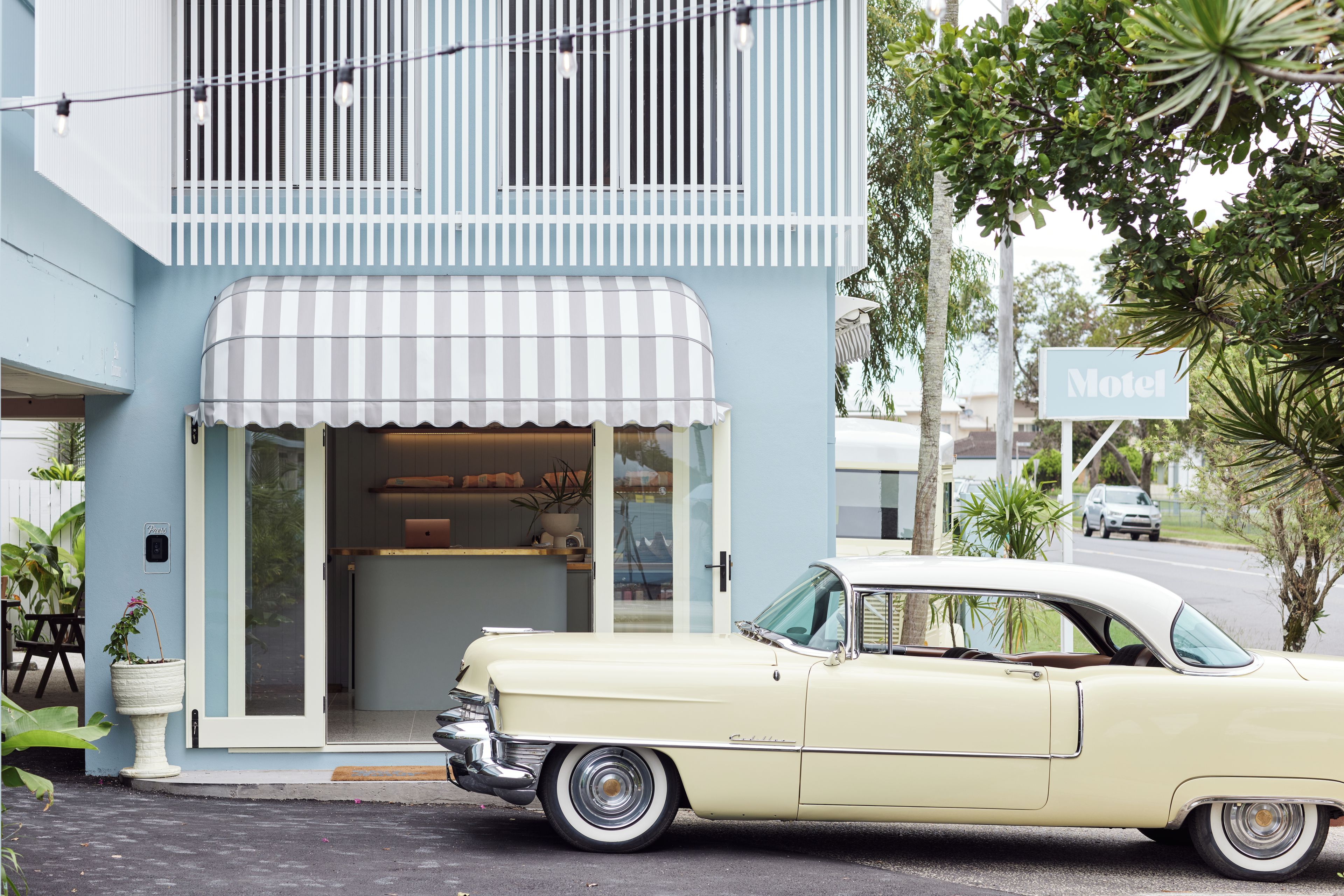 A vintage car parked in front of a hotel with a striped awning and a sign indicating 'Hotel'.