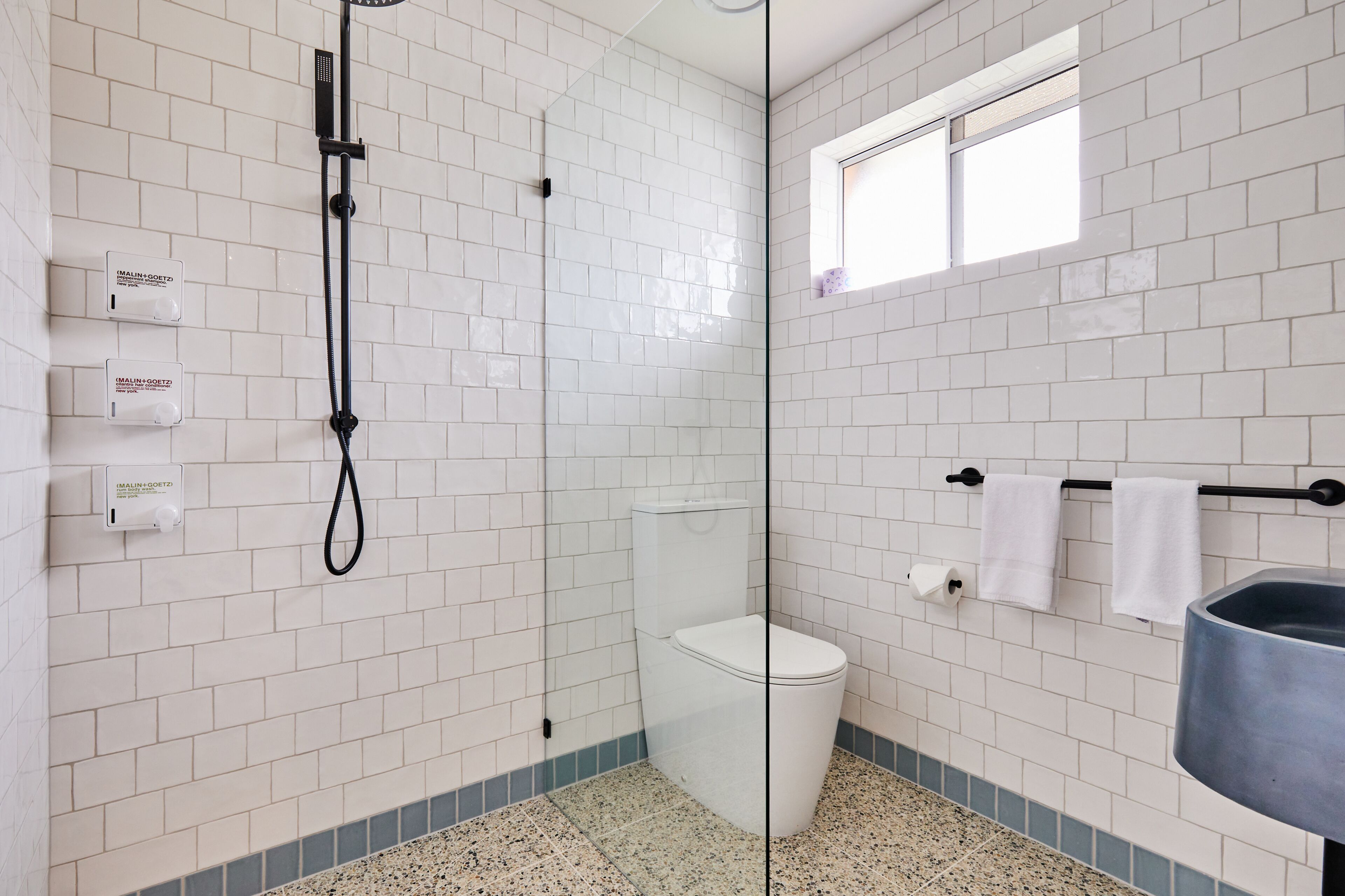 A bathroom with white subway tiles, a glass shower enclosure, a toilet, a sink, and a window.