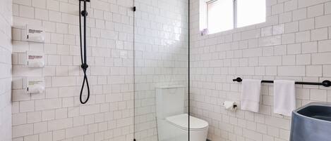 A bathroom with white subway tiles, a glass shower enclosure, a toilet, a sink, and a window.