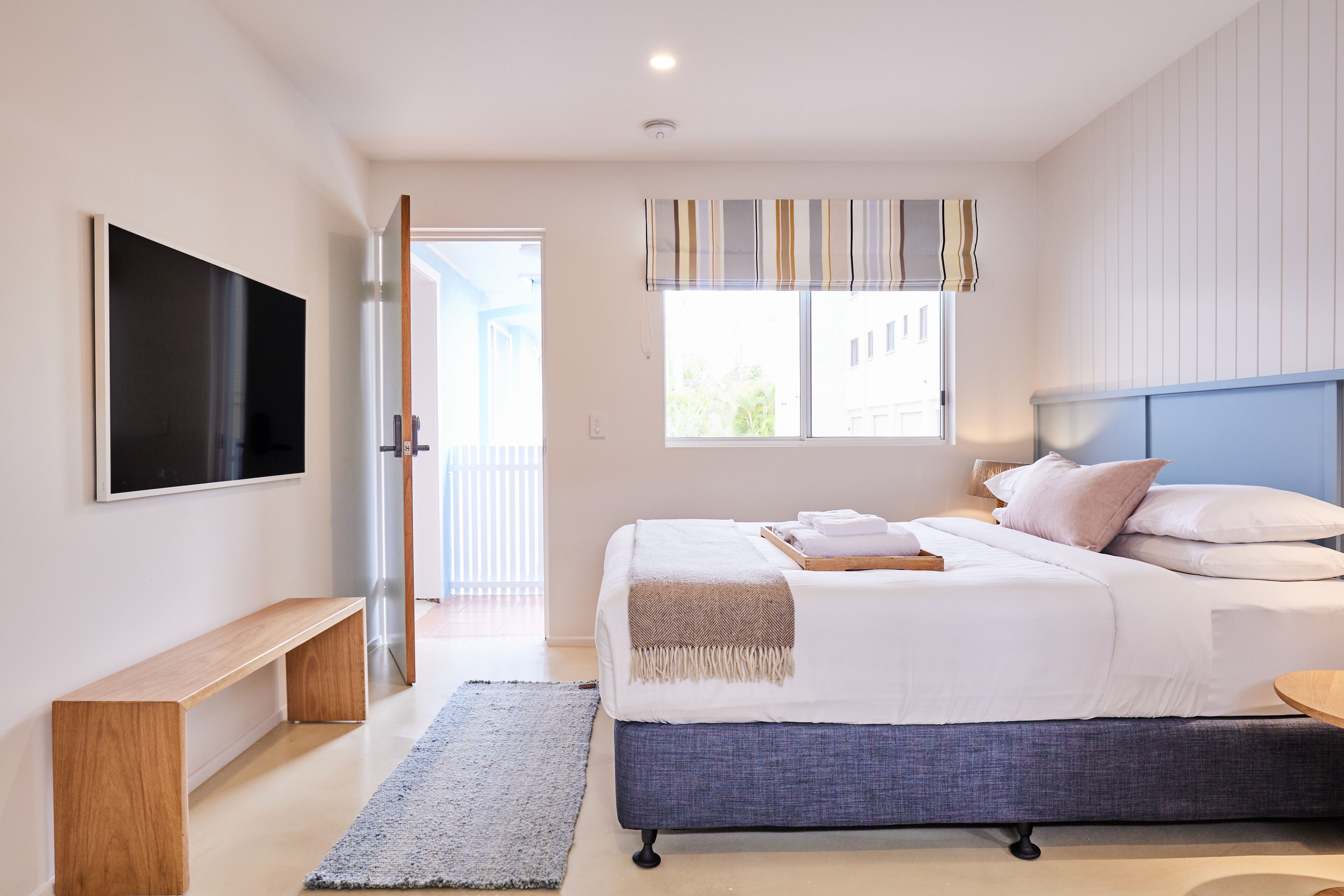 Une chambre à coucher moderne avec un grand lit, un téléviseur fixé au mur et un banc.