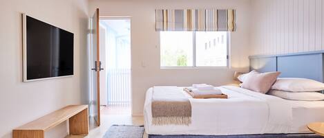 Une chambre à coucher moderne avec un grand lit, un téléviseur fixé au mur et un banc.