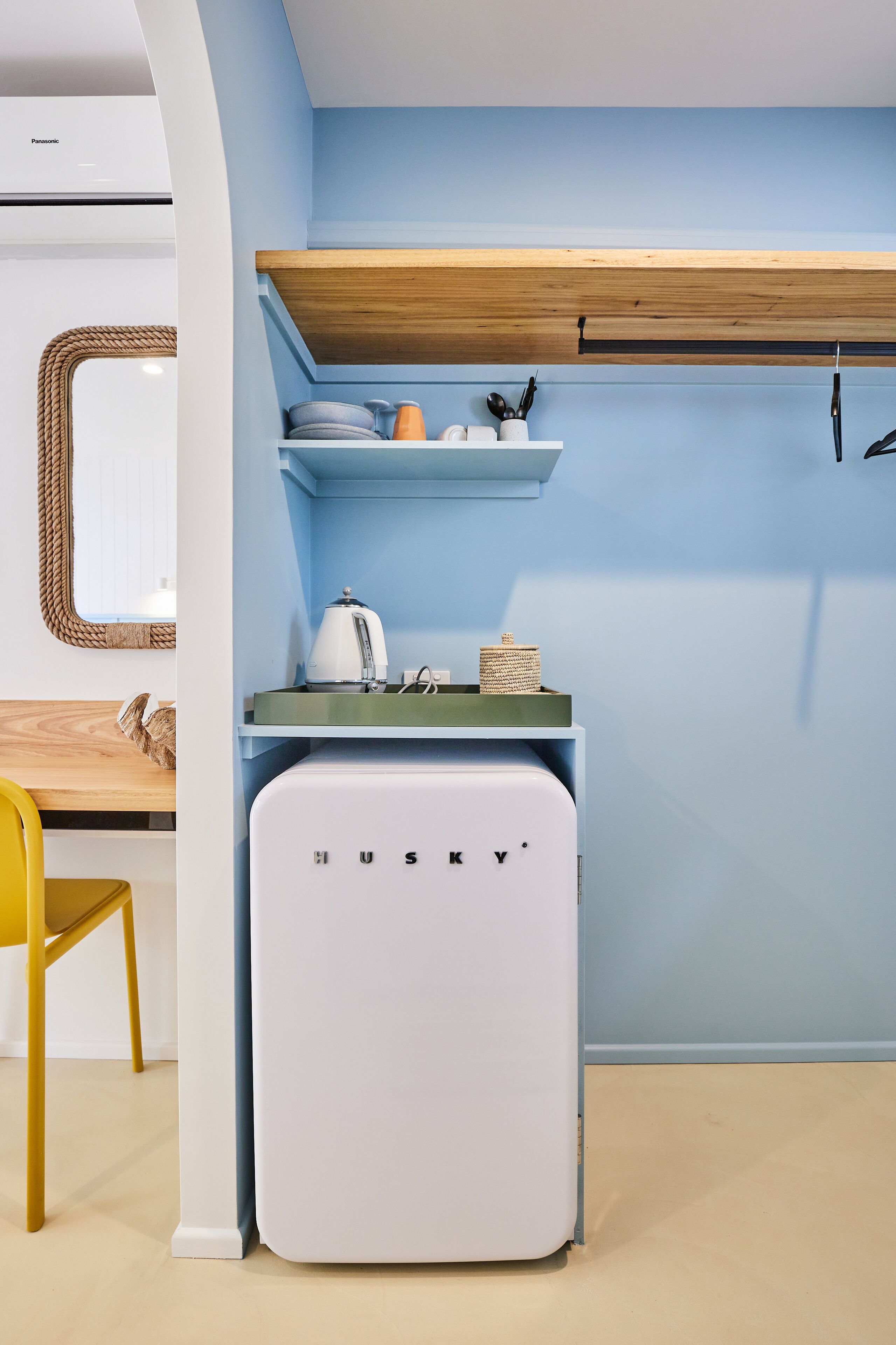 Une cuisine compacte dotée d’un réfrigérateur encastré, d’une étagère en bois et d’un petit plan de travail.
