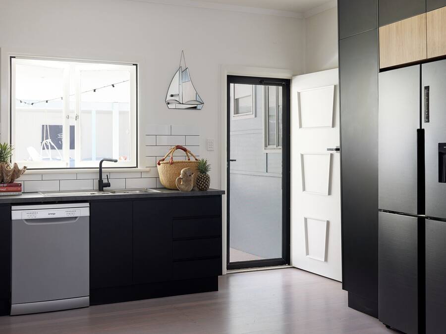 A modern kitchen with a dishwasher, a large window, and a refrigerator.