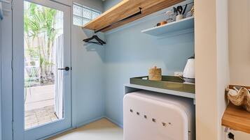 A compact kitchen with a white refrigerator, wooden shelves, and a hanging coat rack.