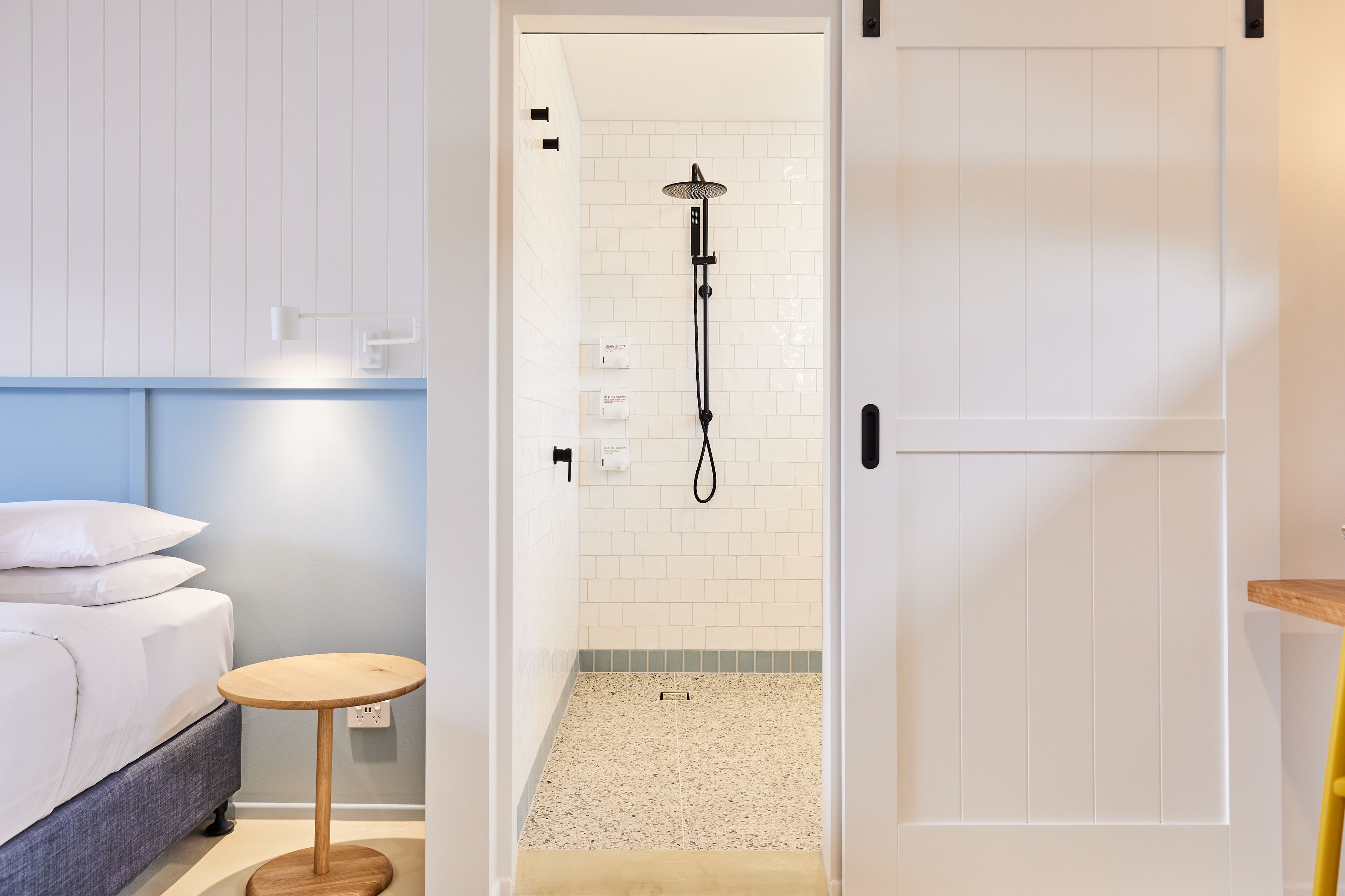 Une salle de bain moderne avec une douche, une petite table ronde et un lit avec du linge de lit blanc.