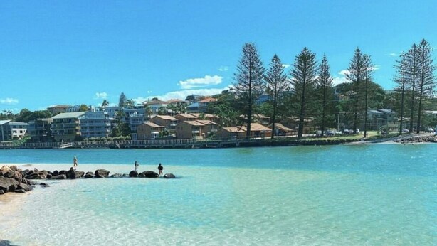 A clear beach with rocky foreground and a residential area in the background. - Blue Water Motel (Kingscliff)