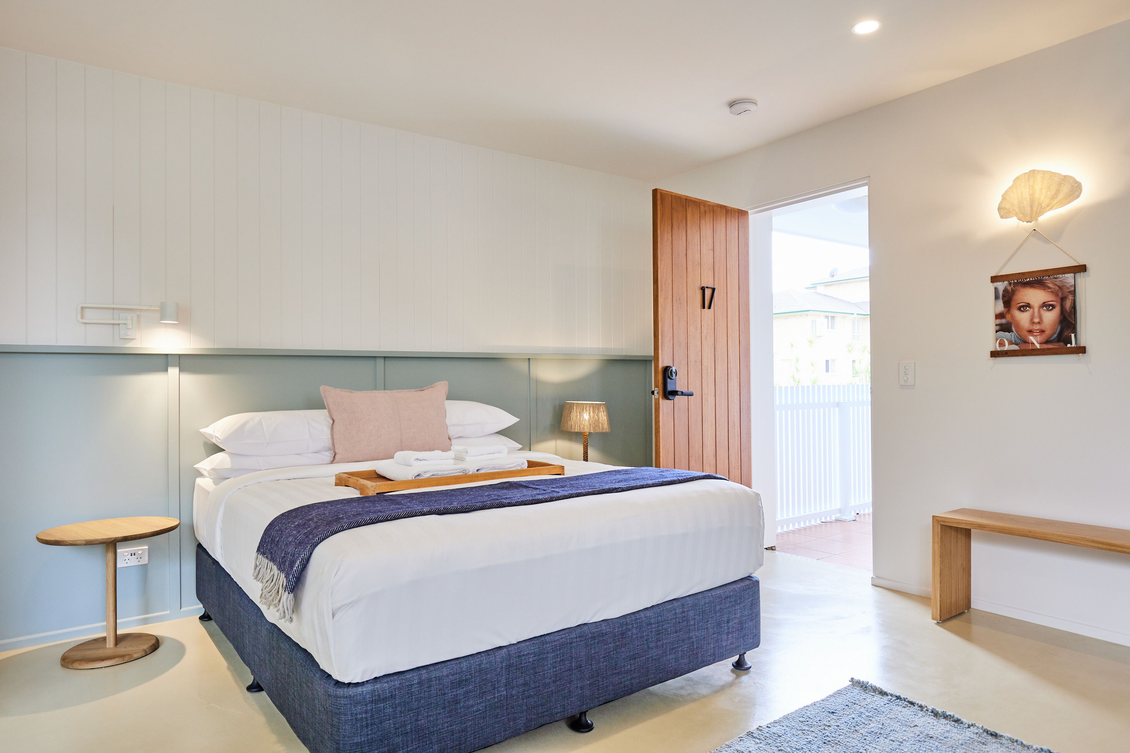 A modern bedroom with a bed, bedside tables, a bench, and a door leading to a balcony.