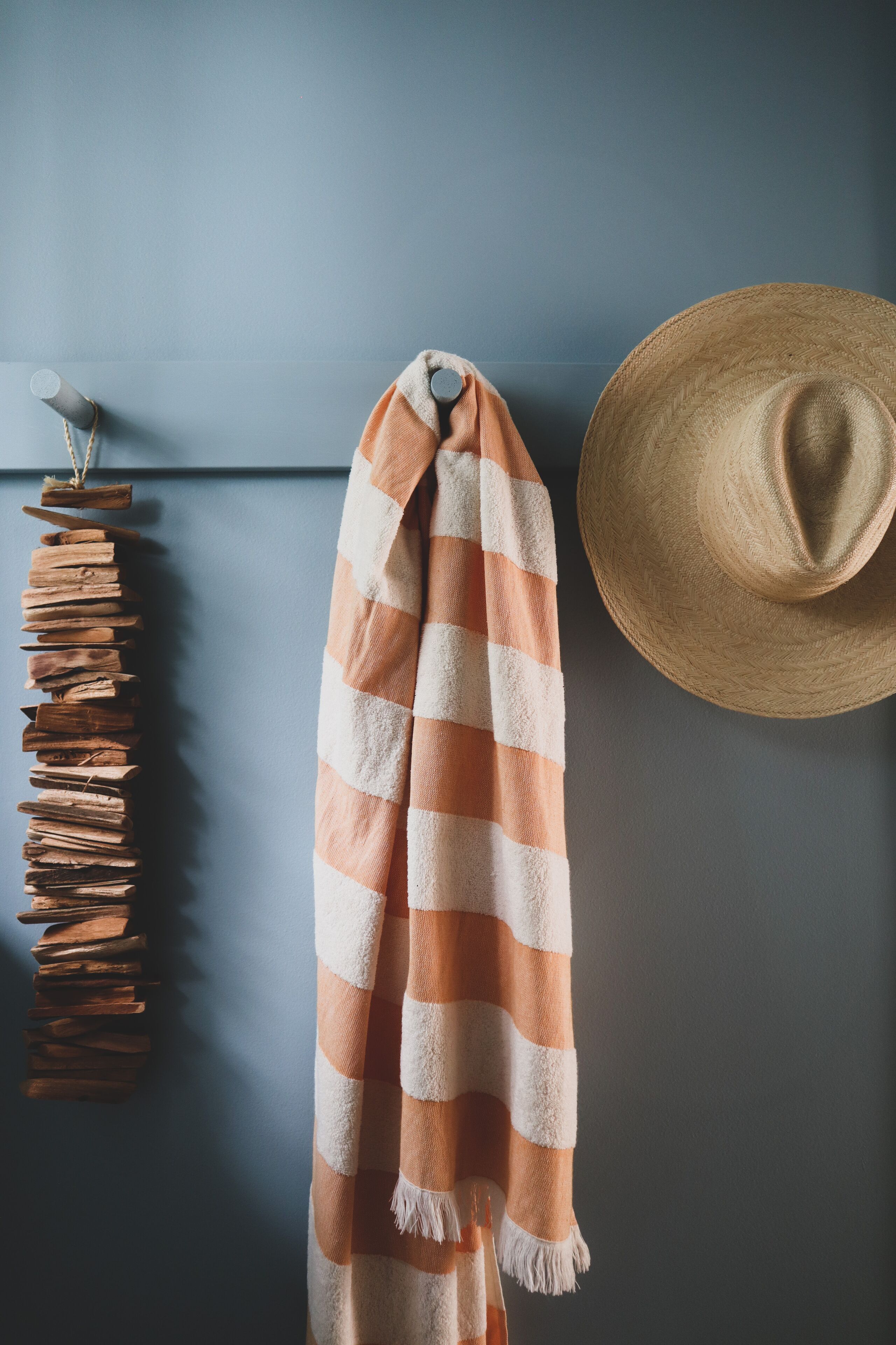 Une serviette à rayures, un chapeau de paille et une pile de blocs en bois, le tout adossé à un mur gris.