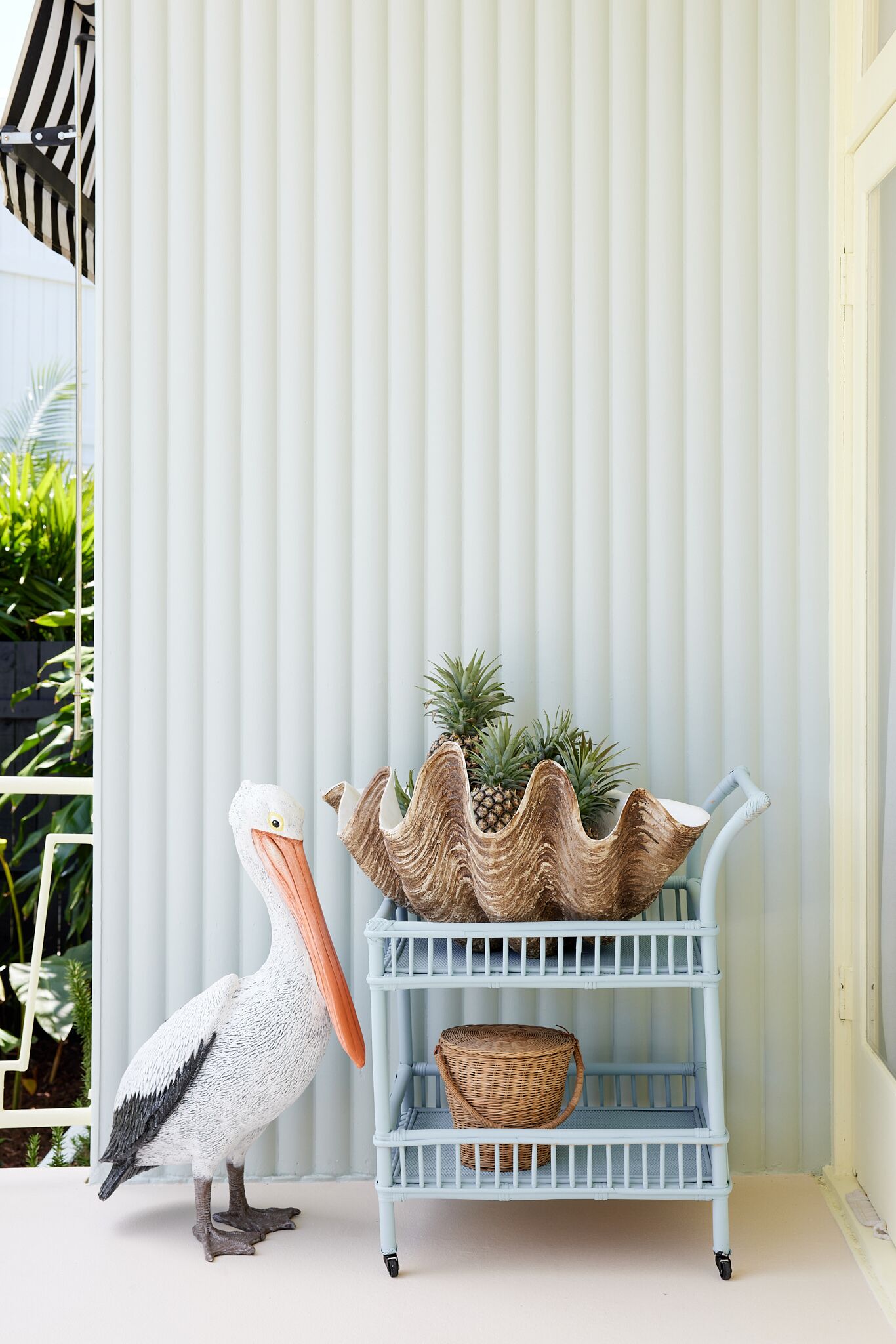 A white pelican sculpture next to a light blue wicker shelf with plants.