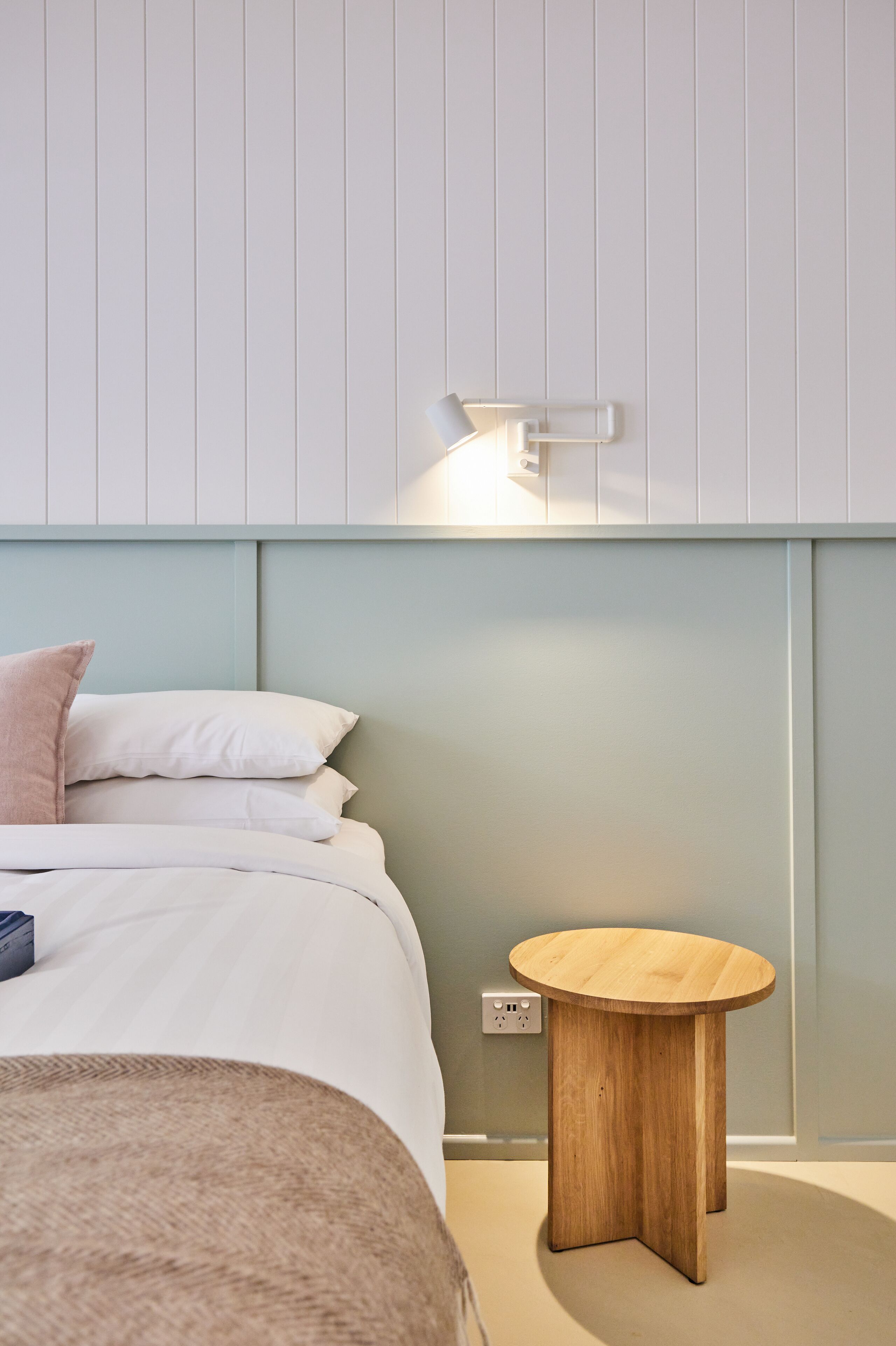 Un dormitorio con cama, almohadas, mesita de noche y una lámpara de pared.