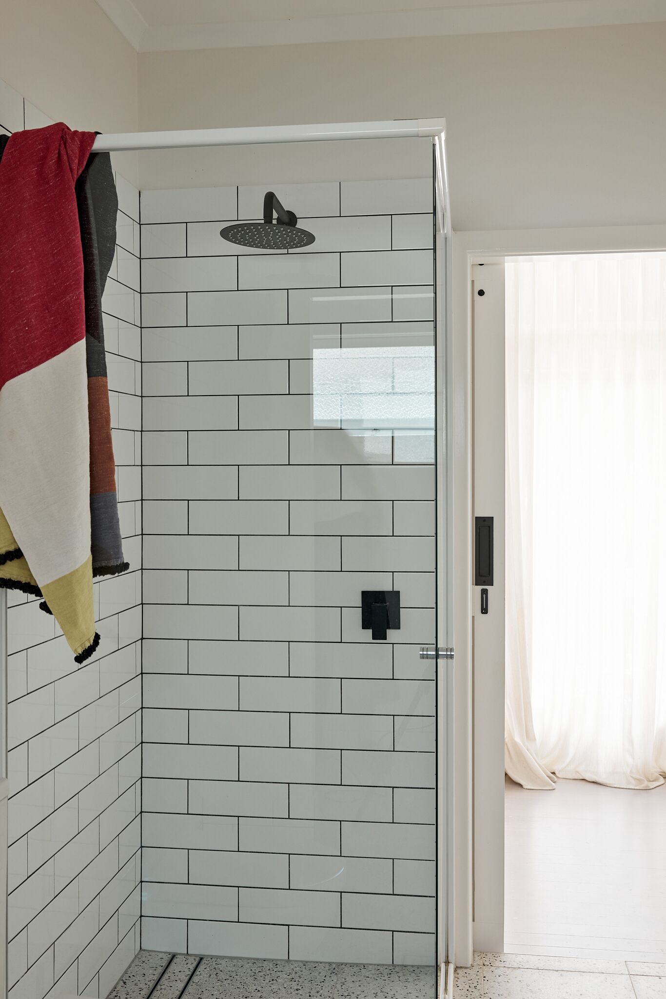 Zona de ducha con paredes de azulejos blancos y puerta de cristal.