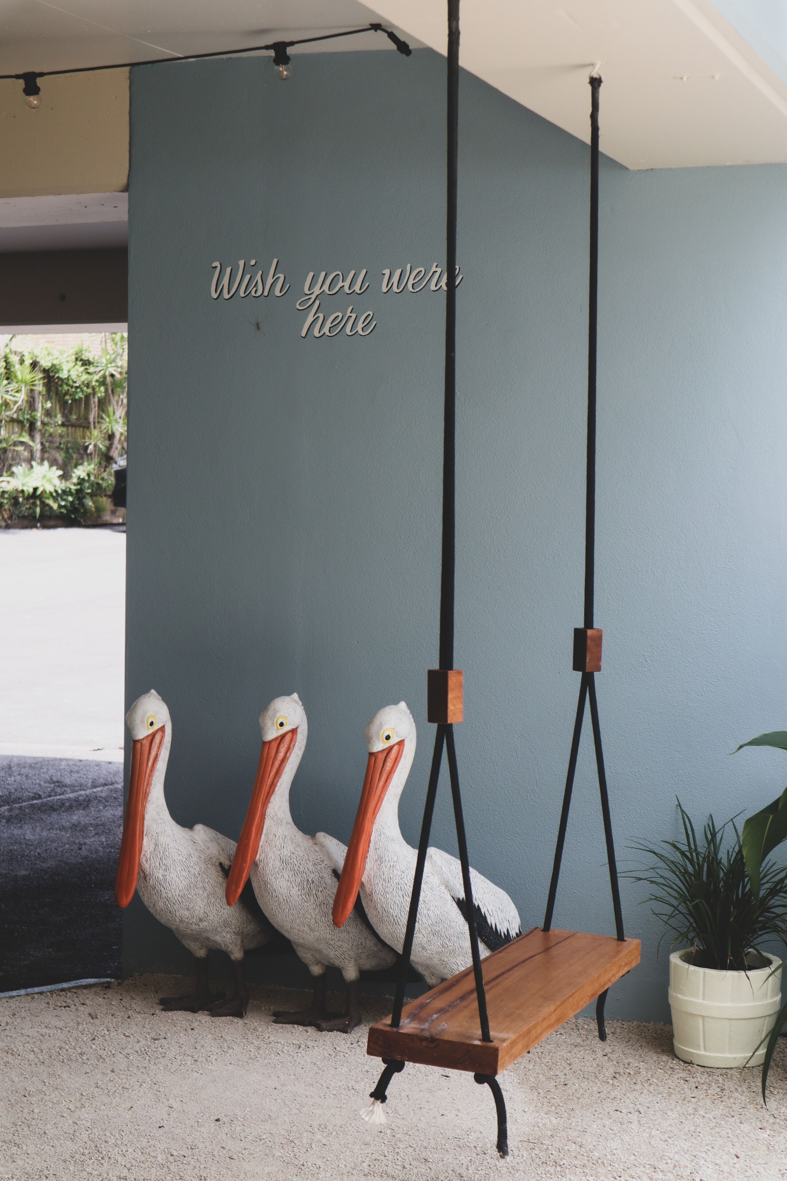 A room with a hanging wooden swing, a wall with a teal color, and three pelican sculptures.