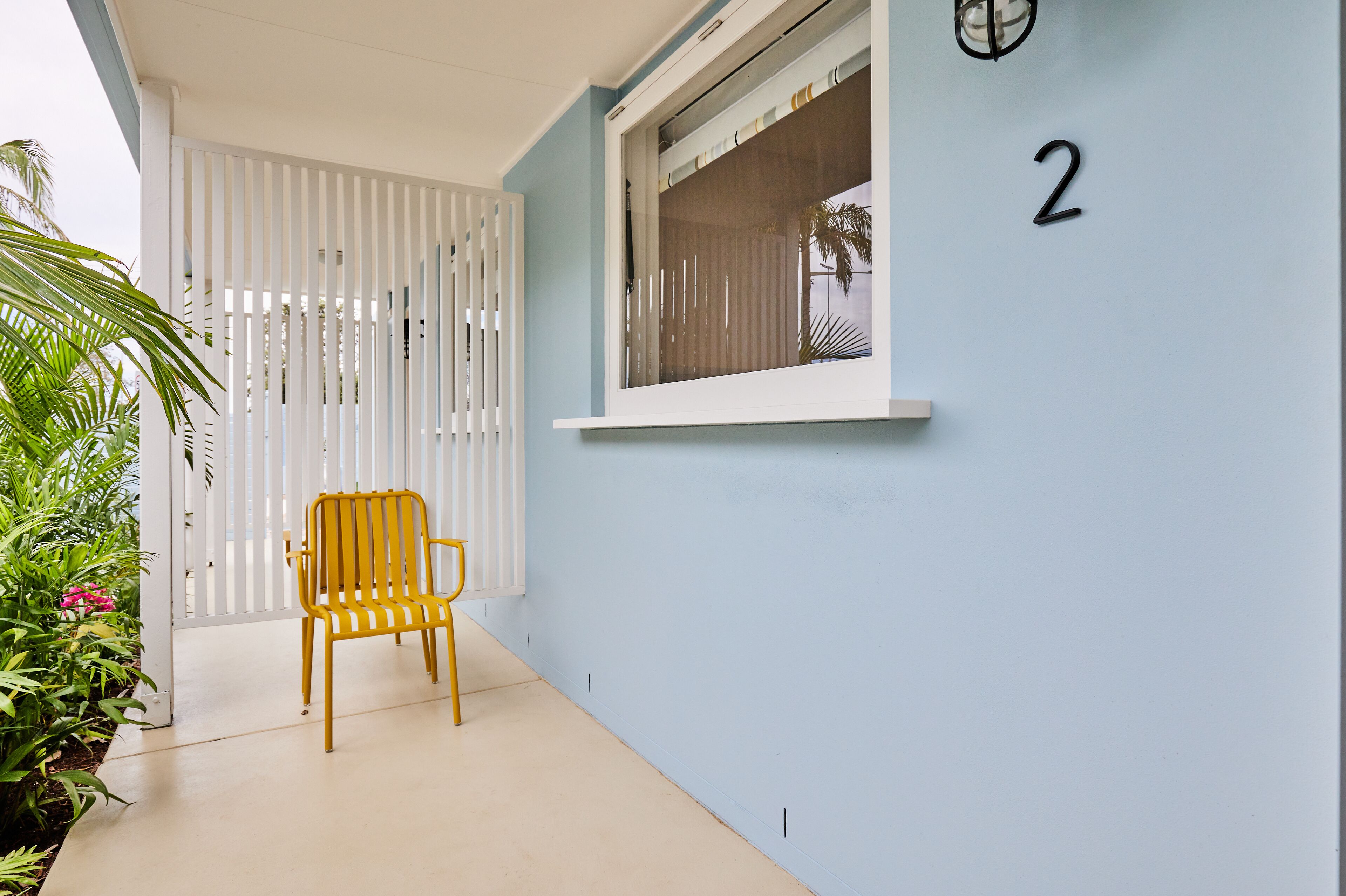 A yellow chair outside a building with a window and the number 2 on the wall.