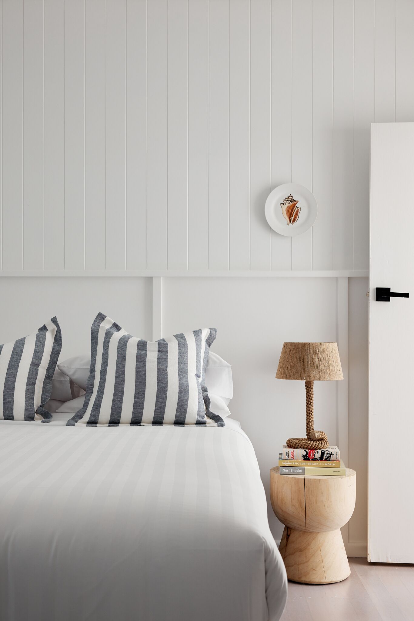 Een netjes opgemaakt slaapkamer met een bed, kussens, een nachtkastje met een lamp en een klein decoratief bord aan de muur.