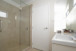 Un baño con cabina de ducha de vidrio, una puerta blanca y un lavabo con artículos de aseo.