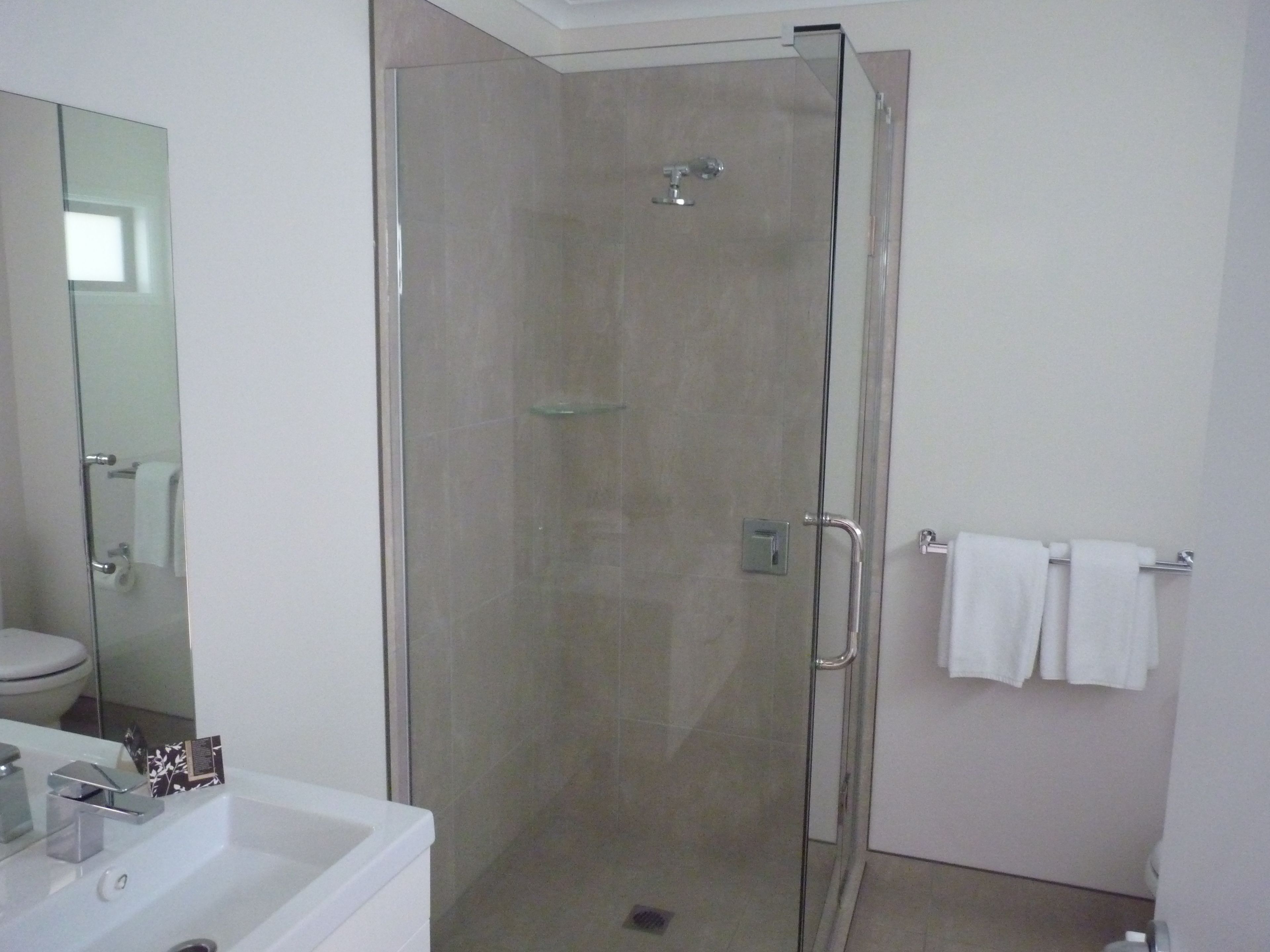 Un baño moderno con ducha de vidrio, lavamanos blanco y espejo.