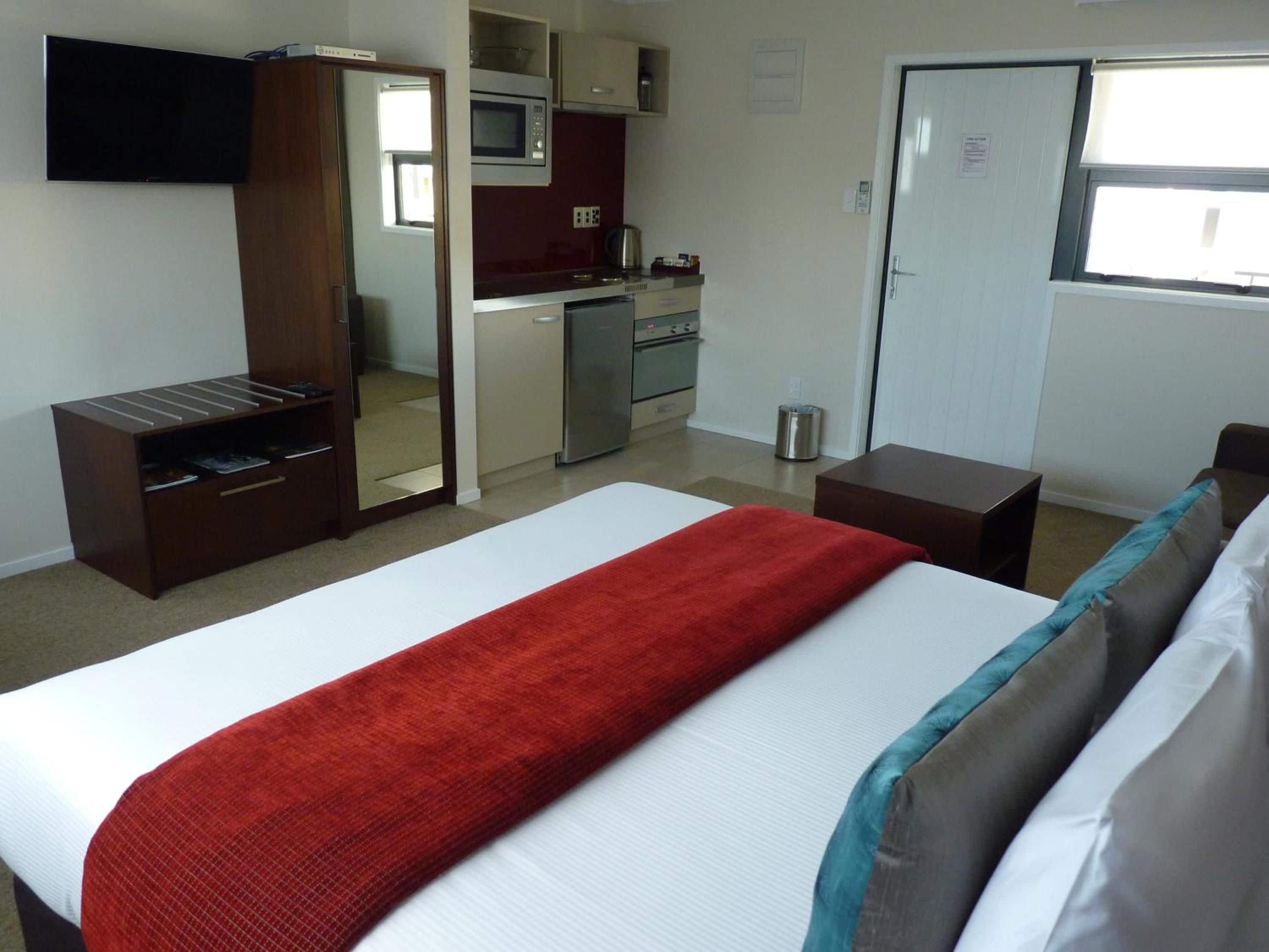A hotel room with a bed, a small desk, a TV, a kitchenette, and a window.