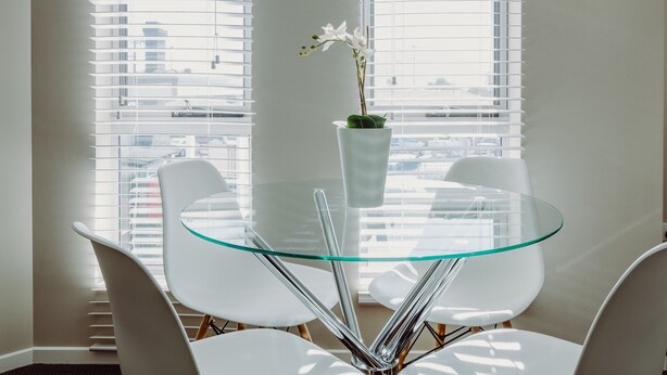A modern dining area with a glass table and white chairs, a vase with an orchid, and a view through large windows. - Crossroads Hotel Narrabri (Narrabri)
