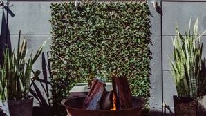 A modern outdoor area with a fire feature, potted plants, and a view of a building with blue shutters. - Crossroads Hotel Narrabri (Narrabri)