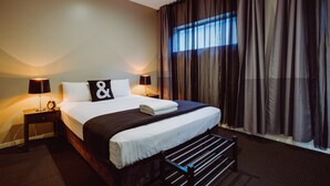 A neatly made bed with white linens and a black and white pillow. There are two bedside lamps on either side of the bed. - Crossroads Hotel Narrabri (Narrabri)