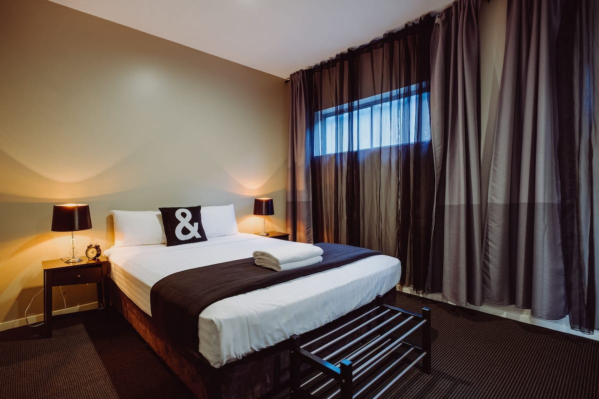 A neatly made bed with white linens and a black and white pillow. There are two bedside lamps on either side of the bed.