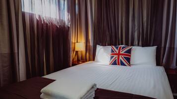 A neatly made bed with white linens and a pillow featuring the Union Jack.