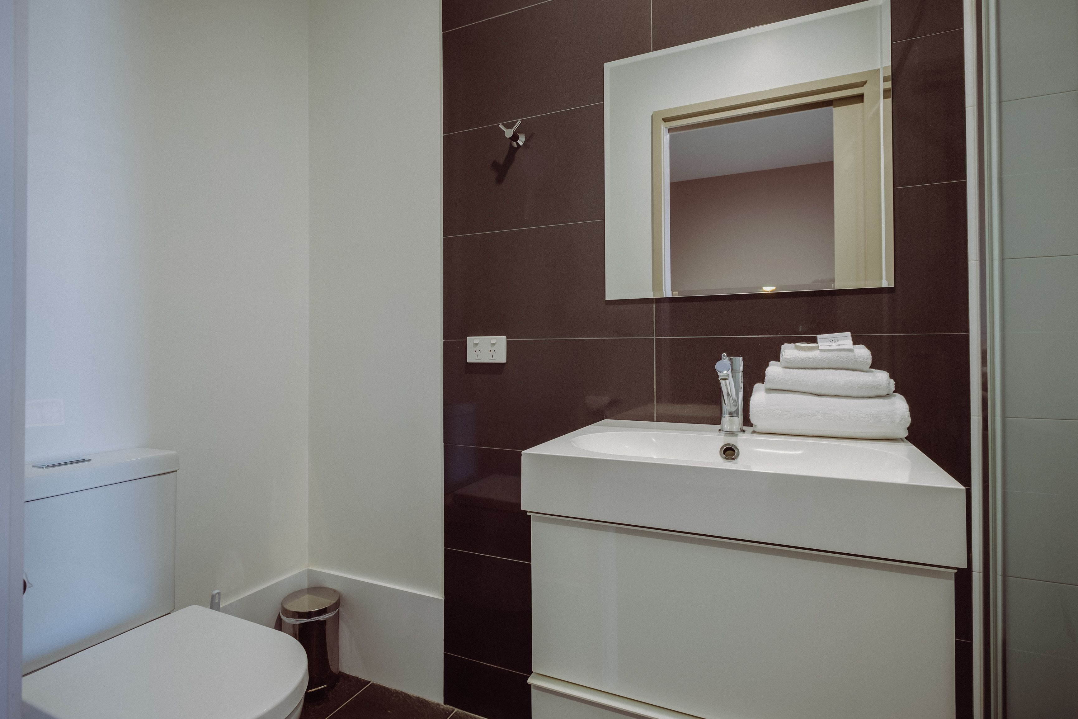 A modern bathroom with a white toilet, a sink with stacked towels, and a mirror above the sink.
