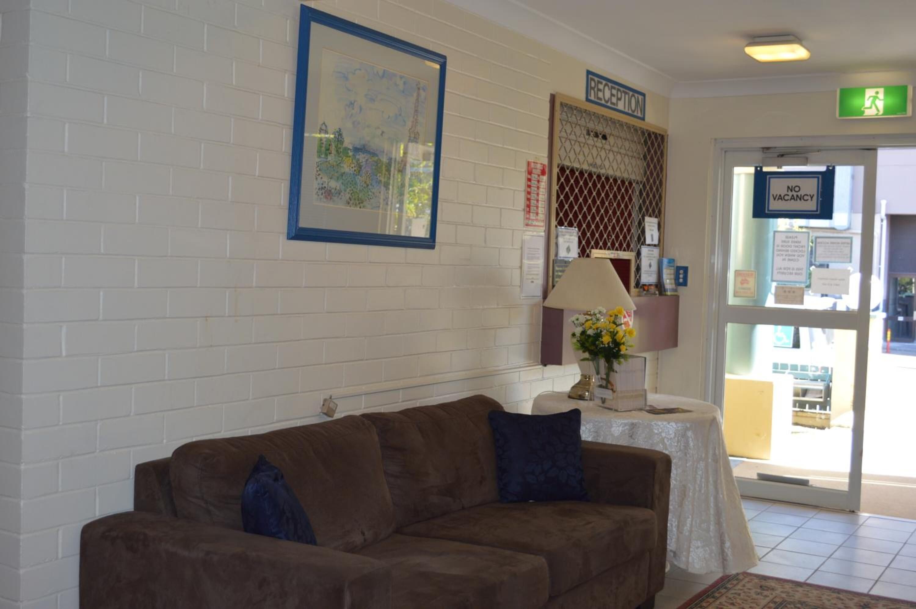 A reception area with a brown sofa, a table with a vase of flowers, and a framed picture on the wall.