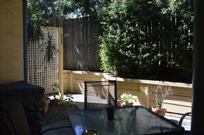 A patio with a glass table and chairs, surrounded by potted plants and a wooden fence. - Tottenham Court Accommodation (Woolloongabba)