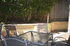 An outdoor patio with a glass-top table and metal chairs, surrounded by a wooden fence and trees. - Tottenham Court Accommodation (Woolloongabba)