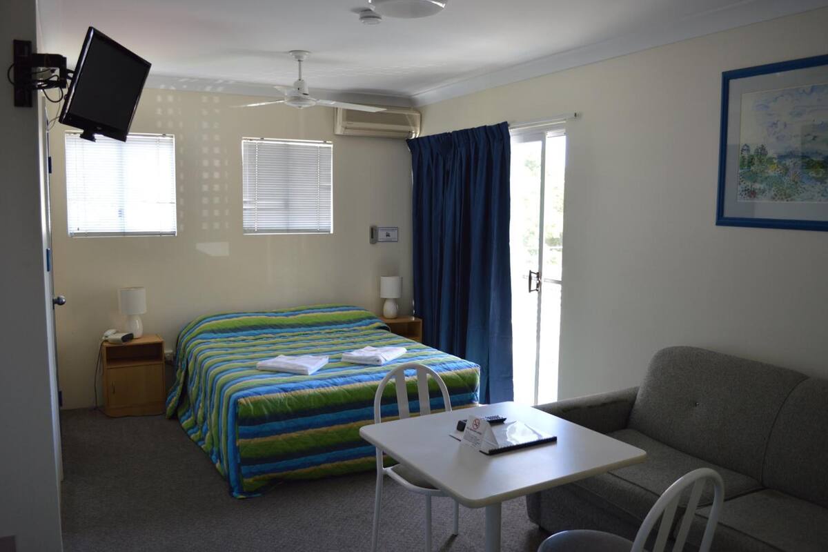 A hotel room with a bed, a desk, a chair, a sofa, a TV, and a window with curtains.