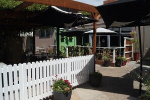 An outdoor seating area with tables and chairs under umbrellas, a white picket fence, and potted plants. - Burkes Hotel Motel (Yarrawonga)