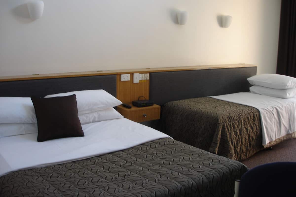 A hotel room with two beds, a wooden headboard, a nightstand with a clock, and wall-mounted light fixtures.