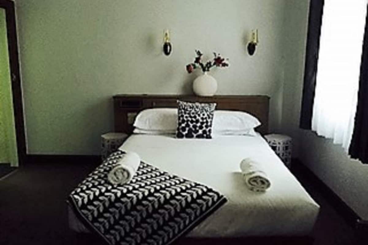 A hotel room with a bed, bedside tables, a nightstand, a vase with flowers, and a window with curtains.