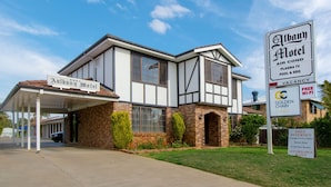 A two-story motel with a covered entrance and a sign indicating amenities like air conditioning, plasma TV, pool & BBQ, and free Wi-Fi. - Aalbany Motel (Narrabri)