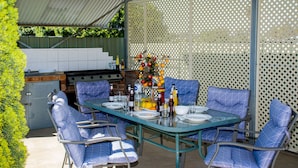 An outdoor patio with a glass table set for dining, surrounded by blue cushioned chairs. - Aalbany Motel (Narrabri)