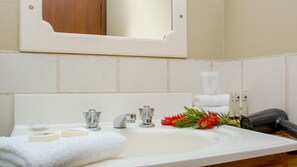 A bathroom with a white sink, two faucets, a mirror, and toiletries. - Aalbany Motel (Narrabri)