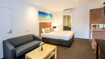 A hotel room with a bed, a sofa, a small table with a vase, a microwave, and a bathroom visible through an open door.