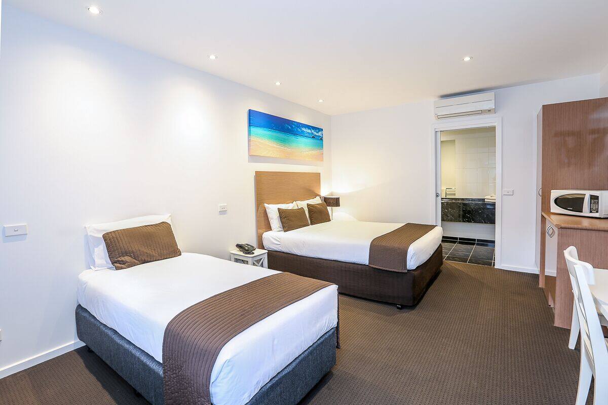 A hotel room with two beds, a desk, a microwave, and a bathroom visible through an open door.