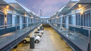 Un edificio moderno con área de estacionamiento techada y un pasillo de vidrio.