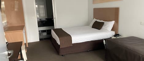 Habitación de hotel con una cama, un escritorio, una silla, un cubo de basura y un cuadro de una playa.