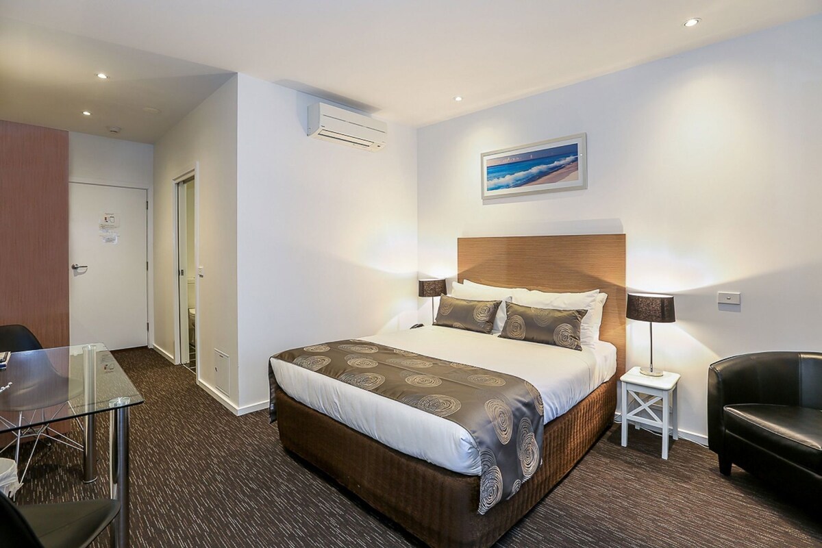 A hotel room with a large bed, bedside lamps, a desk, and a chair.