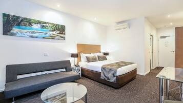 A hotel room with a bed, a sofa, a glass table, and a painting of a waterfall.