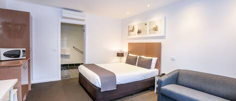 Habitación de hotel con cama, sofá, escritorio con microondas y baño con ducha e inodoro.