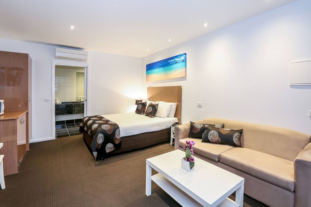 A hotel room with a bed, a sofa, a coffee table, and a painting of a beach.