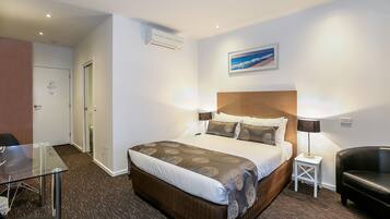 A hotel room with a large bed, a desk, a chair, a small table, and a sofa.