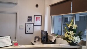 Zona de recepción de un hotel con una araña, certificados enmarcados, un reloj digital y una ventana con vistas.