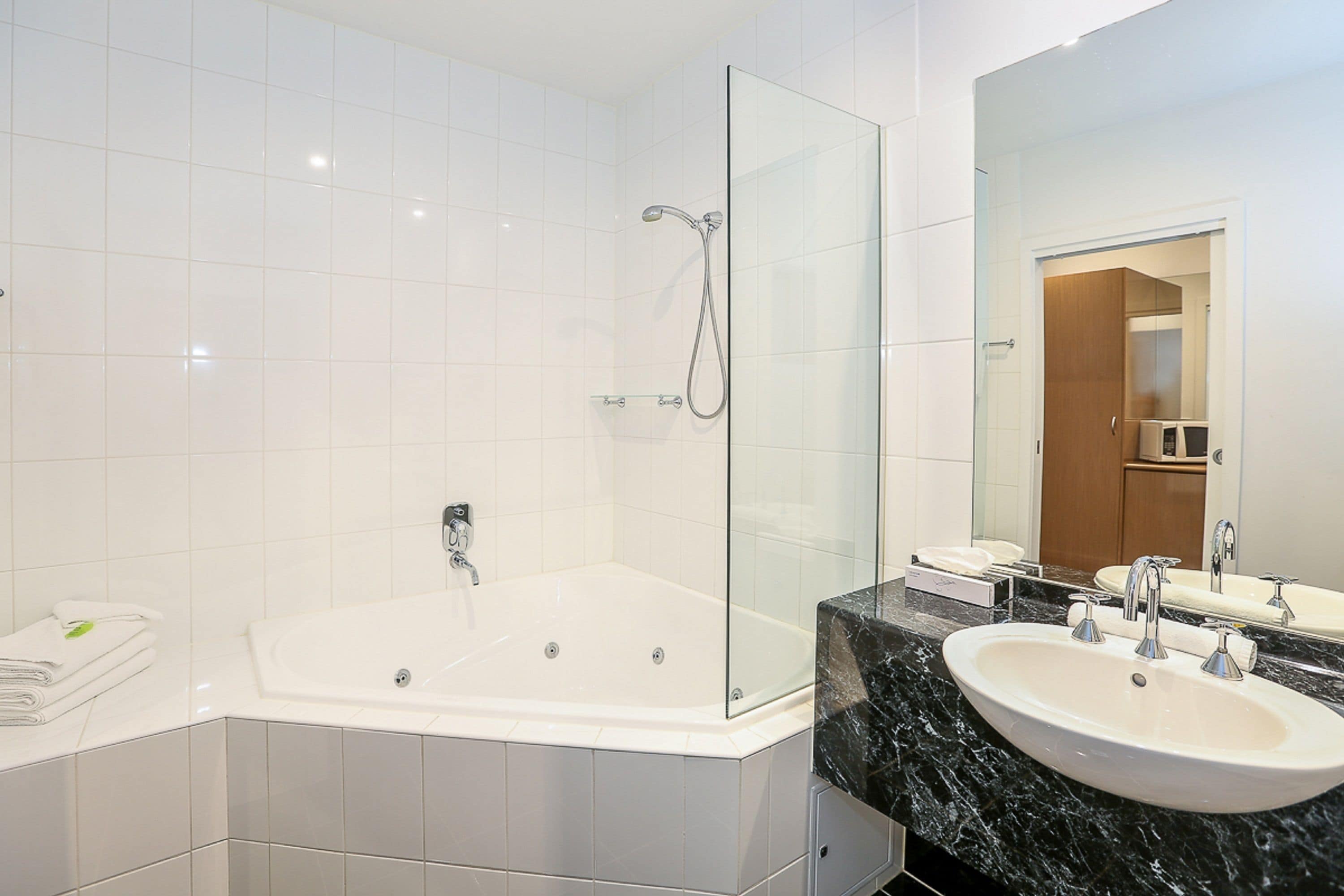Un baño moderno con ducha de vidrio, una bañera amplia y una encimera de mármol con dos lavamanos.